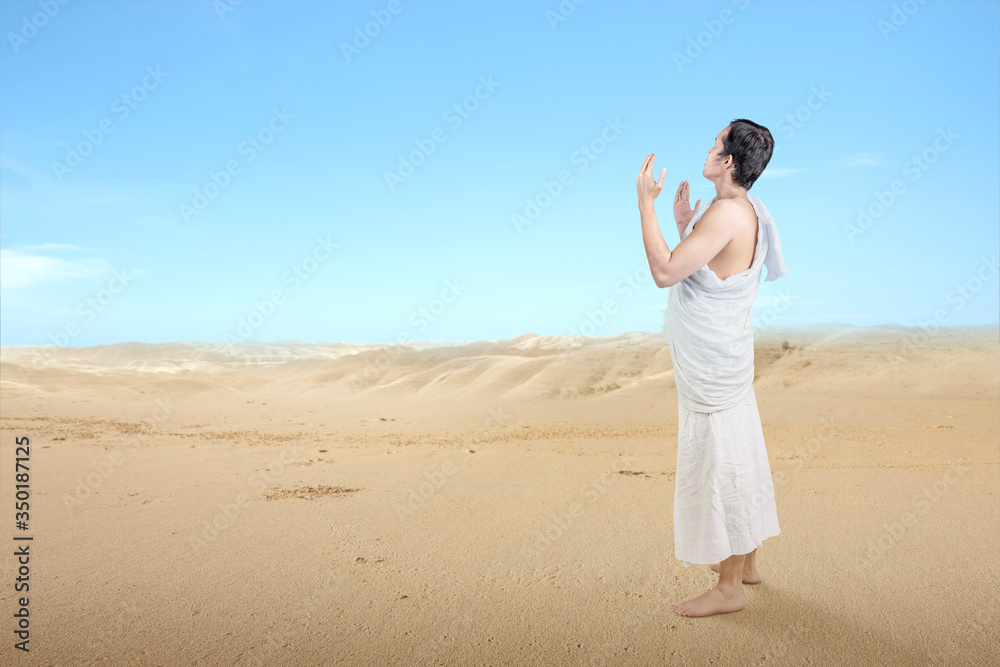 Asian Muslim man in ihram clothes standing and praying while raised arms Asian Muslim man in ihram clothes standing and praying while raised arms