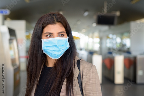 Face of young Indian businesswoman with mask thinking while buying ticket at skytrain station