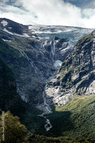 Trip to Norway. Blue ice tongue of Jostedal glacier melts from the giant rocky mountains into the green valley with a lot of waterfalls. Vertical wallpaper © Егор Гангало