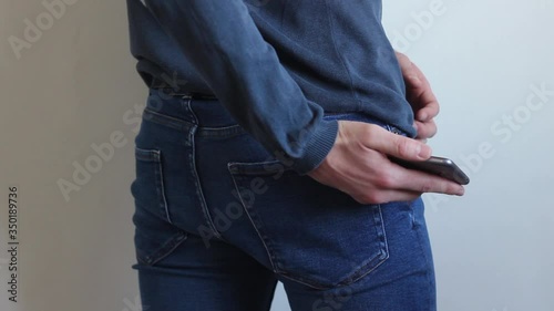 Man takes a phone from his pocket.The young man, turned back to the camera, takes his phone out of the back pocket of his jeans pants, looks at some information and puts it back in his back pocket.
