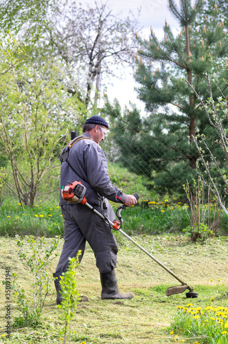 Farmer mows grass in the spring garden. The concept of care for a personal plot.