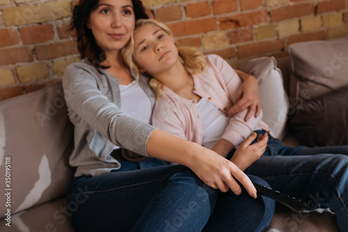 Selective focus of woman holding remote controller and hugging child on couch