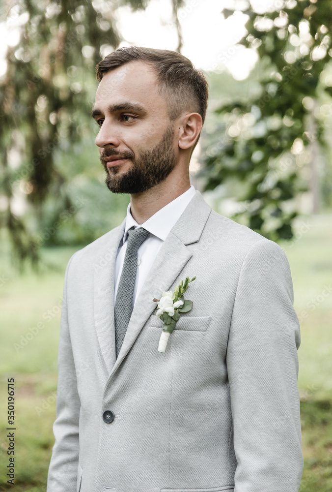 close-up of a groom standing sideways in a gray suit with a small boutonniere close-up of a groom standing sideways in a gray suit with a small boutonniere