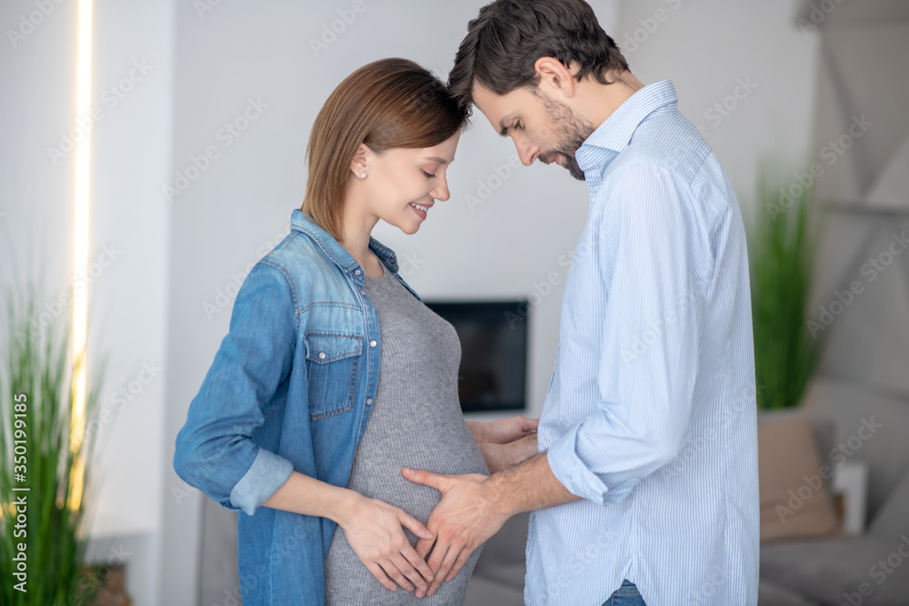 Young dark-haired man touching his wifes pregnant abdomen Young dark-haired man touching his wifes pregnant abdomen
