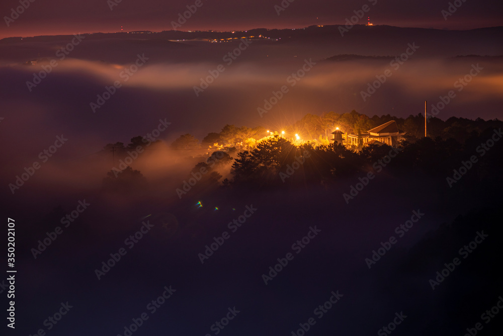 Mountains in fog at beautiful night in autumn in Dalat city, Vietnam. Landscape with Langbiang mountain valley, low clouds, forest, colorful sky with stars, city illumination at dusk. Mountains in fog at beautiful night in autumn in Dalat city, Vietnam. Landscape with Langbiang mountain valley, low clouds, forest, colorful sky with stars, city illumination at dusk.