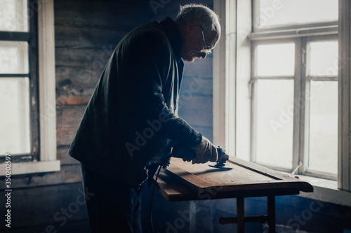 elderly man polishes a wooden board with a grinder at home. Furniture restoration, housework.