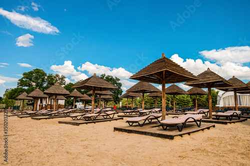 Brown wooden loungers and umbrellas on empty sandy beach. Rows resting places in the failed tourist season. © nskyr2
