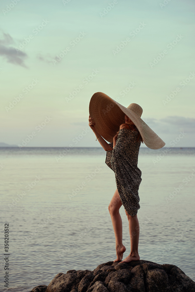 portrait of blonde girl wearing big straw summer hat enjoying sunset