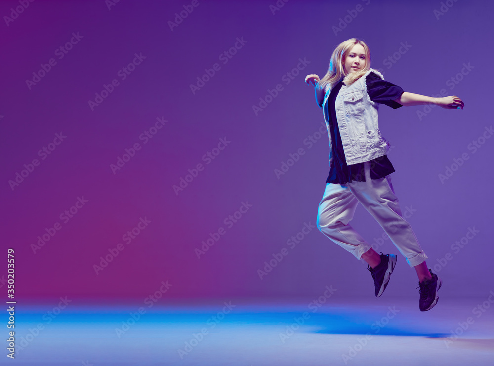 Cute teen girl dancing hip-hop in stylish black and white clothes, in a Studio with neon lighting. Dance color poster.