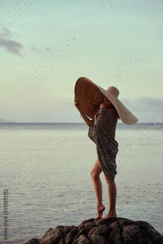 portrait of blonde girl wearing big straw summer hat enjoying sunset