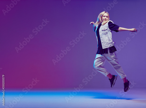 Cute teen girl dancing hip-hop in stylish black and white clothes, in a Studio with neon lighting. Dance color poster. © Georgii