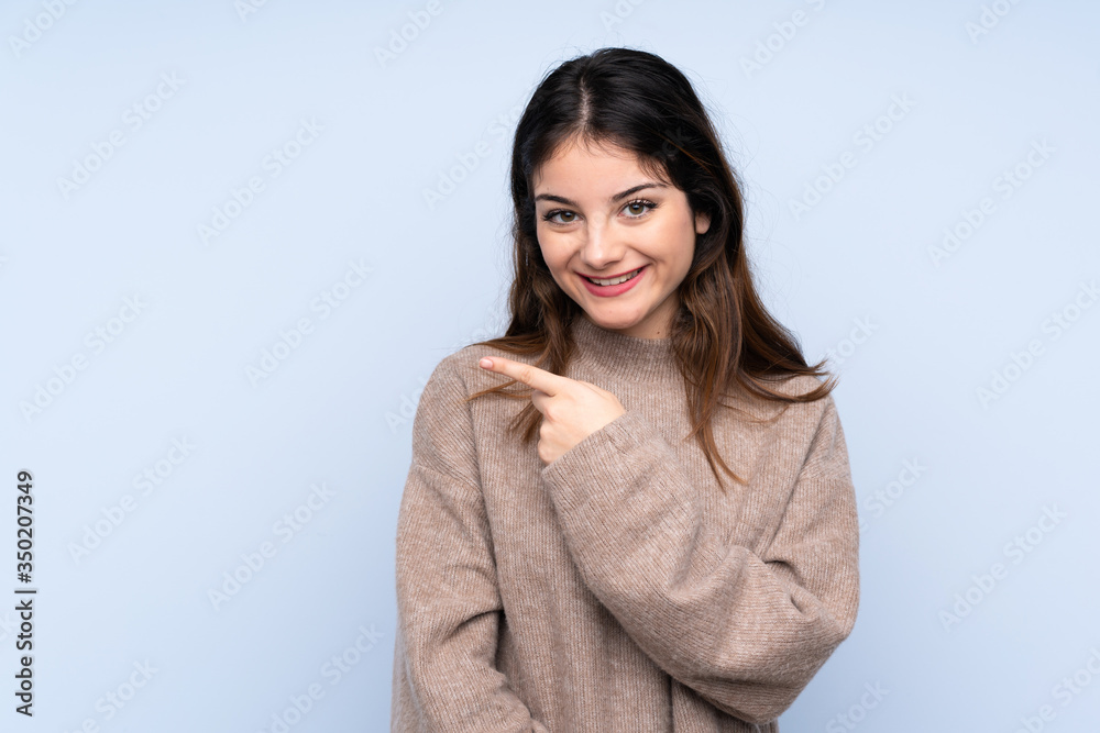 Young brunette woman wearing a sweater over isolated blue background pointing to the side to present a product Young brunette woman wearing a sweater over isolated blue background pointing to the side to present a product