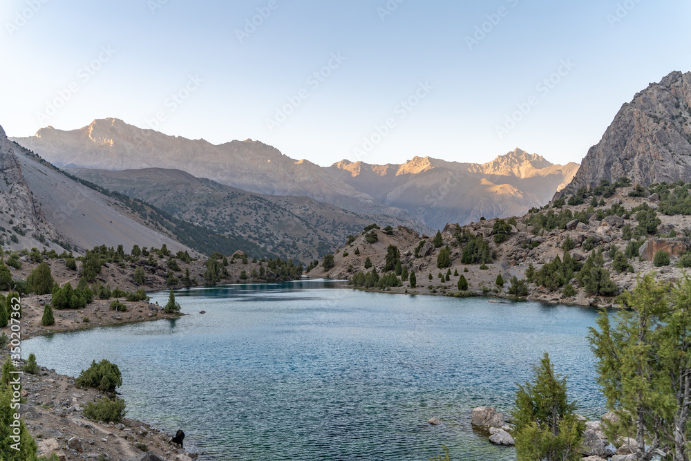 The beautiful mountain trekking road with clear blue sky and rocky hills and the view of Alaudin lake in Fann mountains in Tajikistan