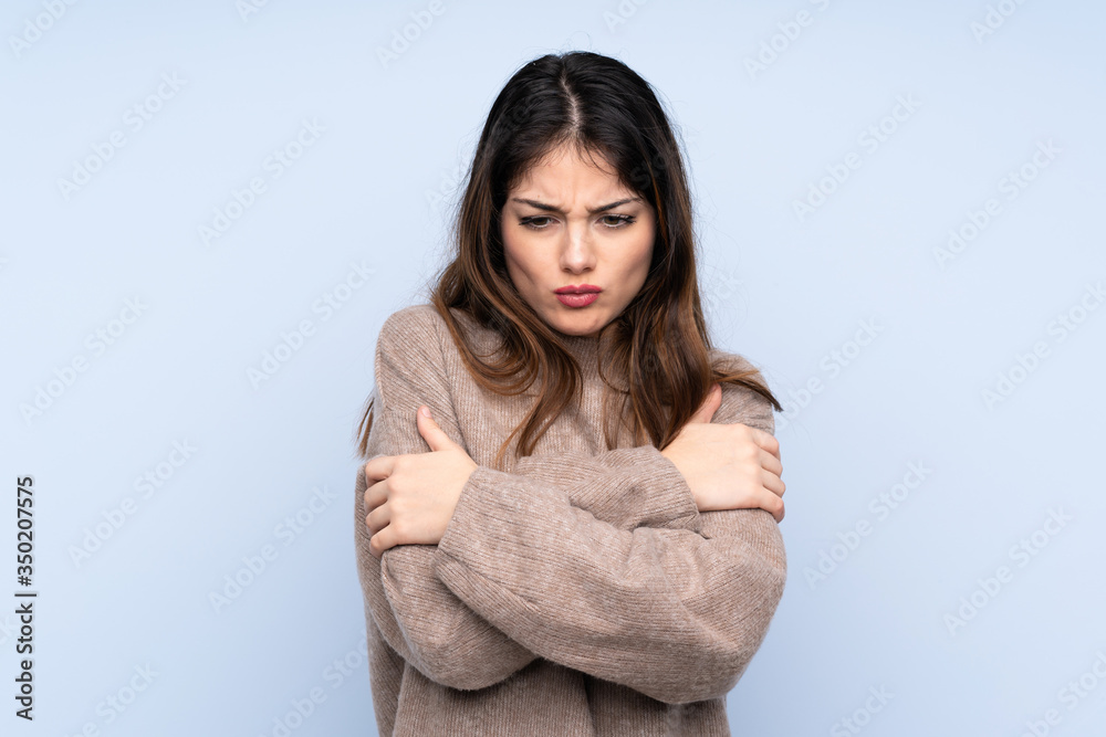 Young brunette woman wearing a sweater over isolated blue background freezing Young brunette woman wearing a sweater over isolated blue background freezing