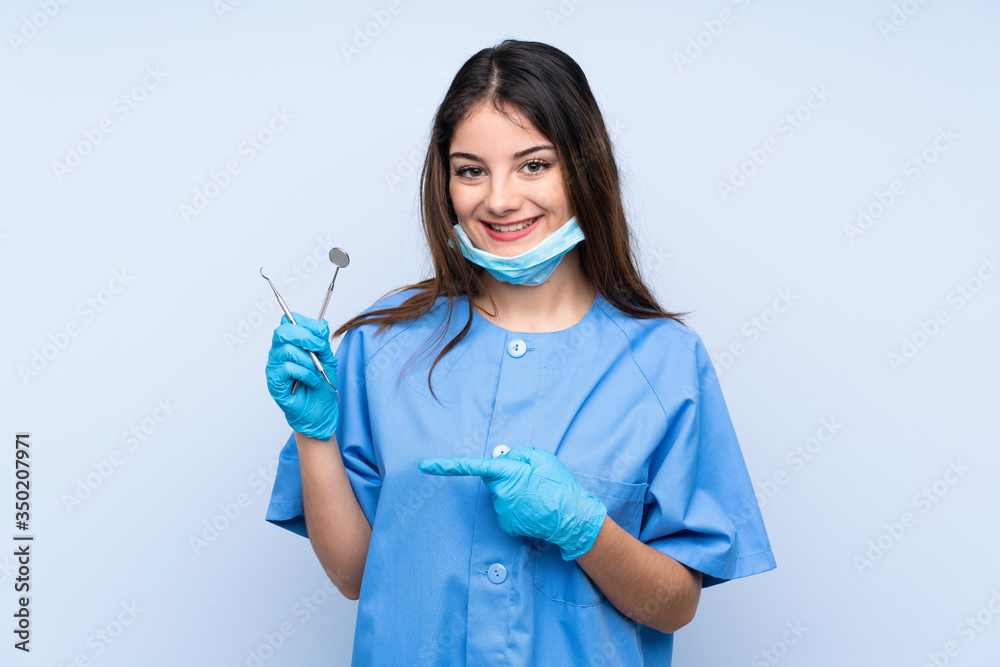 Woman dentist holding tools over isolated blue background pointing finger to the side Woman dentist holding tools over isolated blue background pointing finger to the side