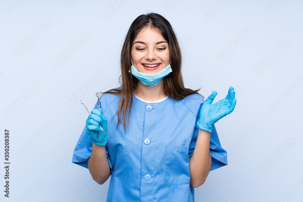 Woman dentist holding tools over isolated blue background laughing