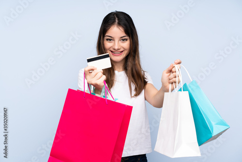 Young brunette woman over isolated blue background holding shopping bags and surprised