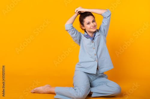 Smiling young girl in pajamas home wear posing while resting at home isolated on yellow background studio portrait. Relax good mood lifestyle concept. © satura_