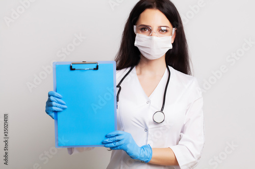 Doctor in a gloves, mask and glasses holds a blank form with space for text