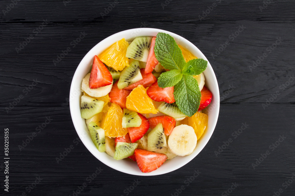 Fruit  salad in the white bowl In the center of  the black wooden  background. Top view. Copy space.