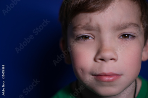 portrait of a pensive nine year old blond boy on a blue background