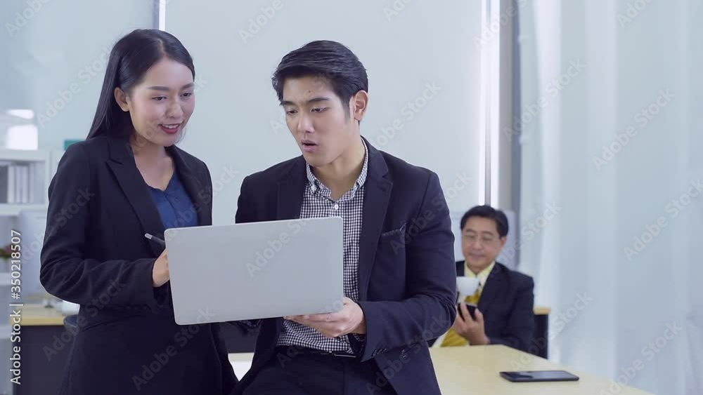 Happy young Asian Business people stand to discuss marketing information In the laptop computer in the office that looks modern Happy young Asian Business people stand to discuss marketing information In the laptop computer in the office that looks modern