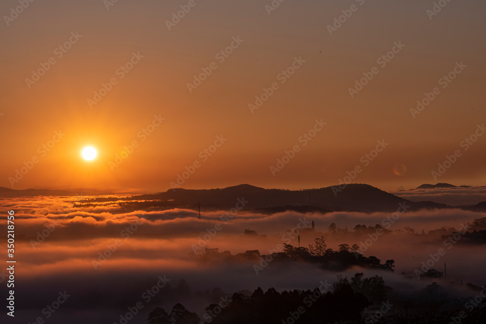 Obraz premium Mountains in fog at beautiful morning in autumn in Dalat city, Vietnam. Landscape with Langbiang mountain valley, low clouds, forest, colorful sky , city illumination at dusk.