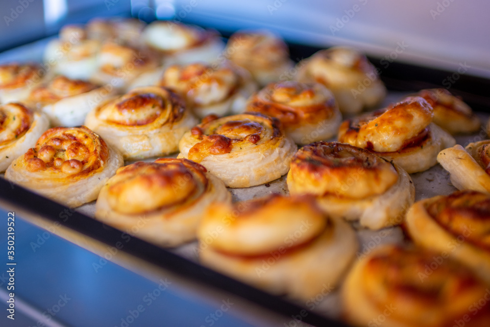 Freshly baked, crispy, salty snails from puff pastry with ham and cheese in the oven