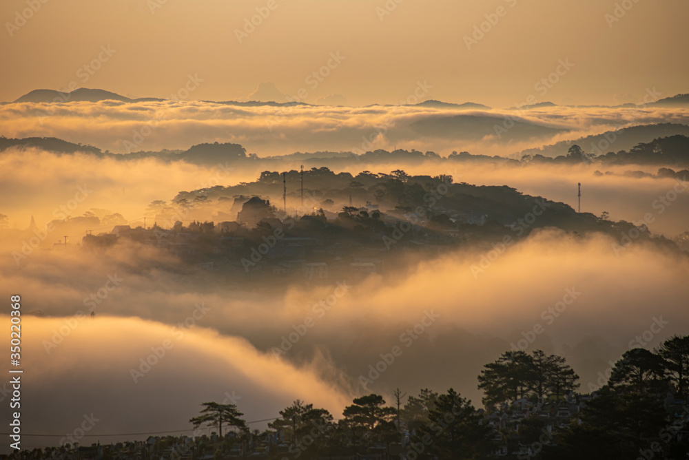Obraz premium Mountains in fog at beautiful morning in autumn in Dalat city, Vietnam. Landscape with Langbiang mountain valley, low clouds, forest, colorful sky , city illumination at dusk.
