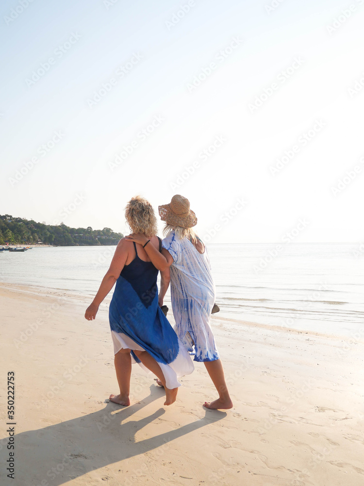 Senior women walking barefoot at sea shore at sunrise. Vertical photo Senior women walking barefoot at sea shore at sunrise. Vertical photo
