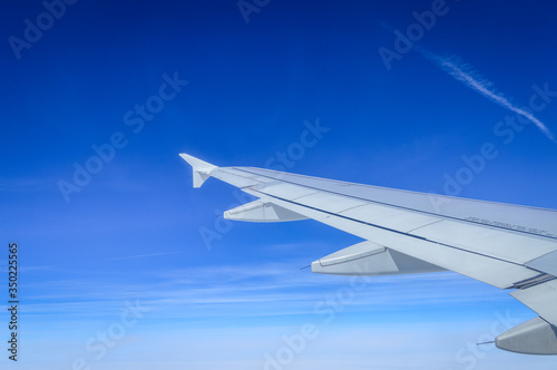 View over the clouds from the porthole of an airplane with plane wing and blue sky