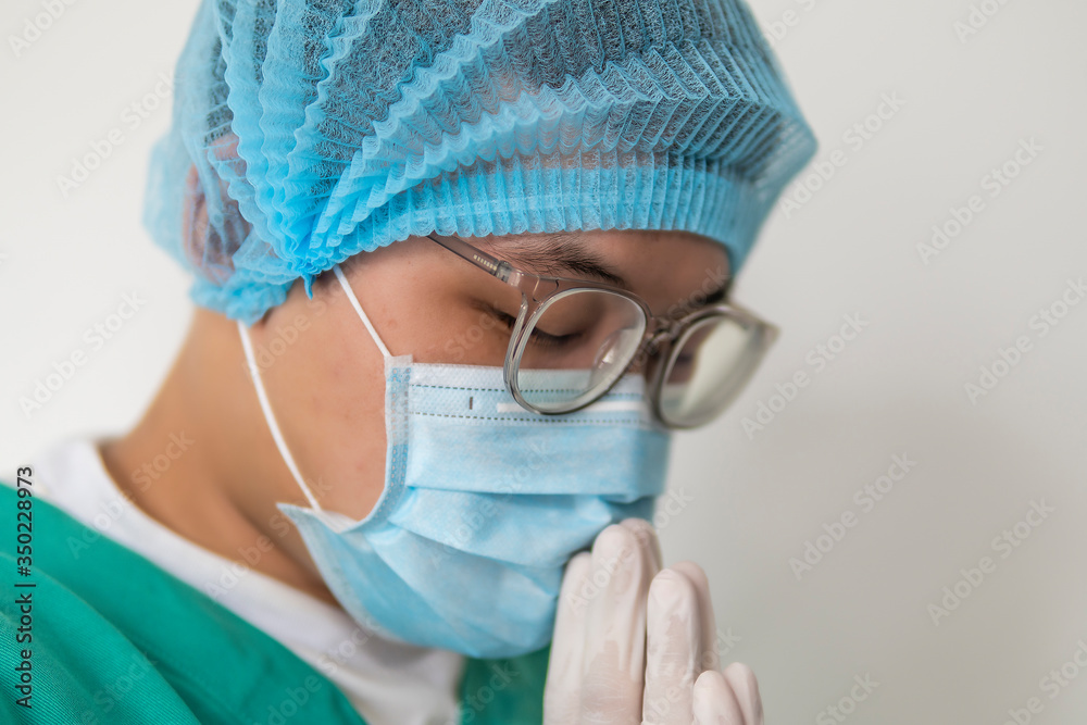 Fototapeta premium Tired praying doctor at the hospital. A doctor, a nurse who is thinking about treating a disease and a pandemic. Surgeon after surgery. Coronavirus, covid-19 concept
