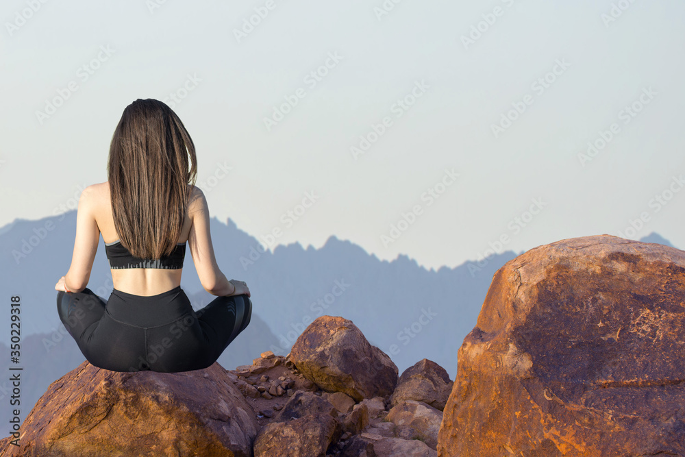 A thin athletic girl takes a break between classes on the background of mountains in the early morning, enjoys silence and freedom.