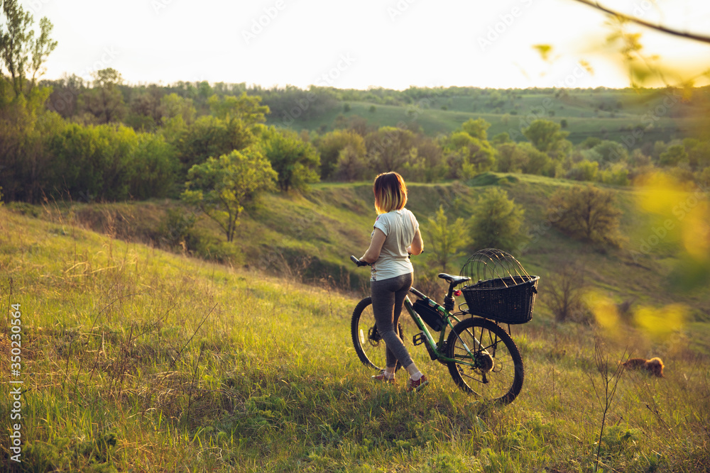 Obraz premium Young woman having fun near countryside park, riding bike, traveling with companion spaniel dog. Calm nature, spring day, positive emotions. Sportive, active leisure activity. Walking together.