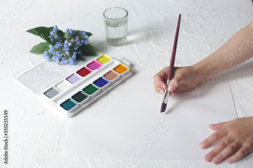 Children's hand holds a brush and paints.
