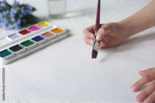 Children's hand holds a brush and paints.
