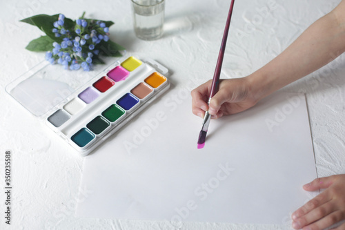 Children's hand holds a brush and paints.
