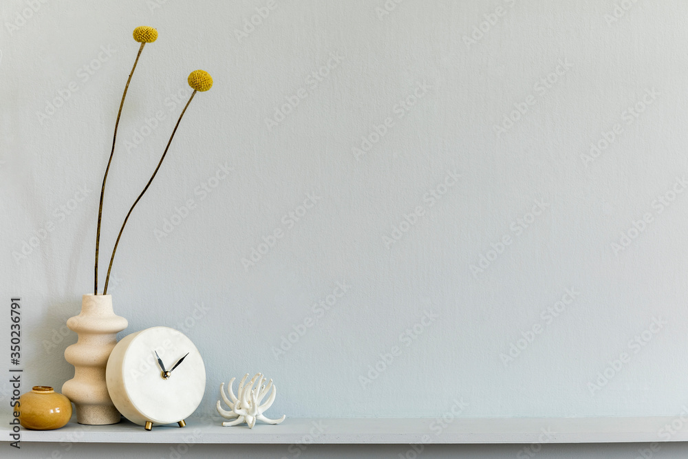 Minimalistic composition on the shelf with dried flower in design vase, white clock and accessories. Grey wall. Copy space.