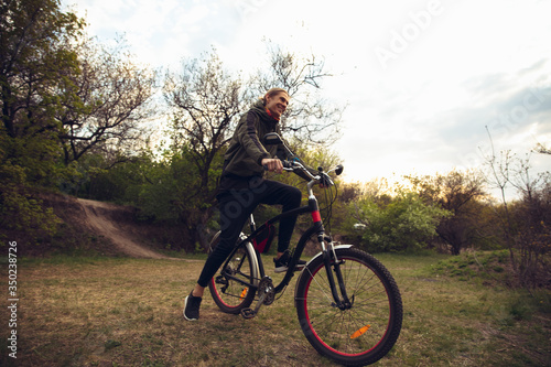 Young man having fun near countryside park  riding bike  traveling at spring day. Calm nature  spring day  positive emotions. Sportive  active leisure activity. Walking in motion  blossoming nature.