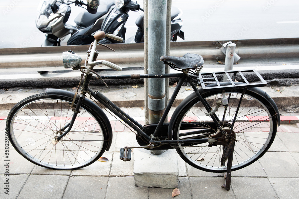 Obraz premium Black antique bicycle parked on a foot bath beside an electric pole