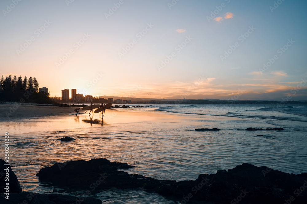 Beautiful sunset behind surfers, casting glow over beach and waves. Coolangatta, Queensland, Australia.