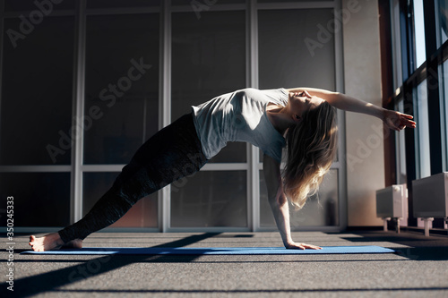 A young girl with light hair does an asana with a bend in the back leans on her legs and one hand, the second hand is raised up