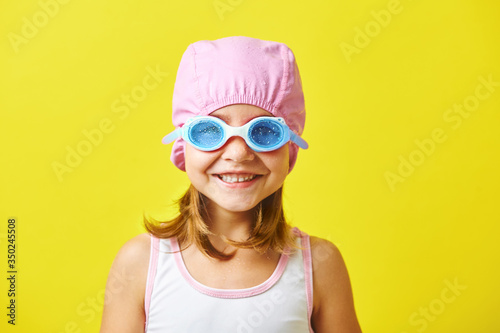 Smiling little girl in swimming cap and glasses on colored background. © Ilshat