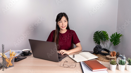 A young, beautiful relaxing business asian girl use a laptop working remotely from home on desk as a freelancer, quarantine for Coronavirus and smart working concept.