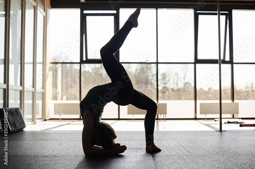 Silhouette of a young woman practicing the concept of yoga, performing a handstand, against the background of panoramic Windows