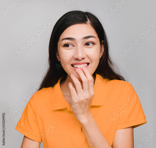 young beautiful asian woman, long black hair, wore orange t shirt, show Secretly face,crafty on gray background