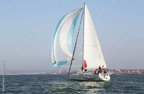 White motor yacht with raised sails takes part in the training regatta. A strong wind tipped the ship. Increase small wave of emotion in the competition. On the horizon you can see the city and the bl