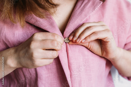 Girl fastens a button on a pink pajamas shirt made of linen, beautiful home clothes. Cozy bathrobe. Natural fabric. Homewear