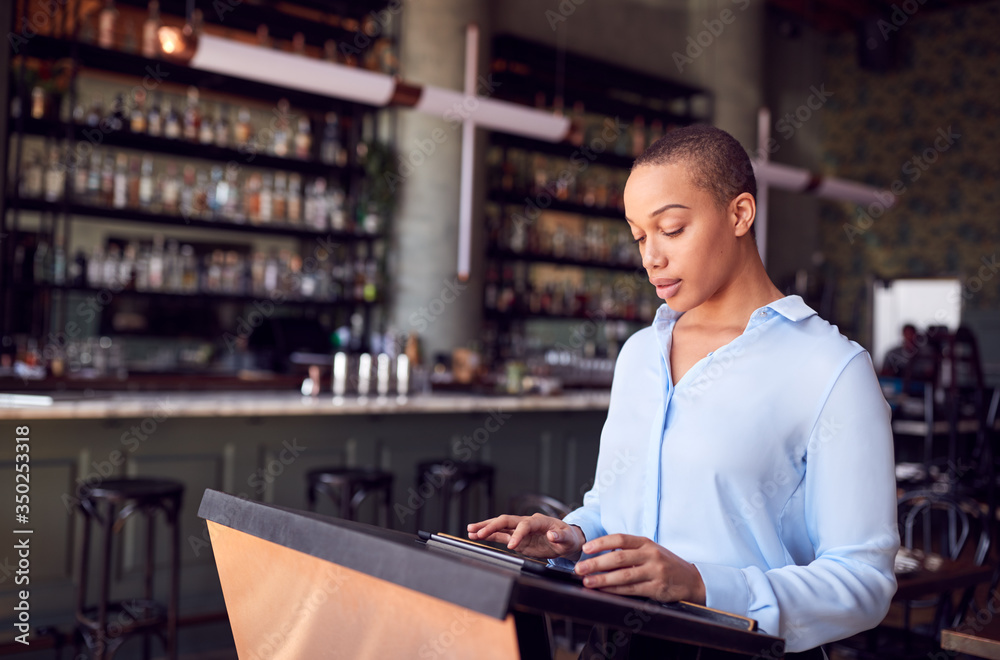 Female Owner Of Restaurant Bar Standing At Counter Using Digital Tablet Female Owner Of Restaurant Bar Standing At Counter Using Digital Tablet