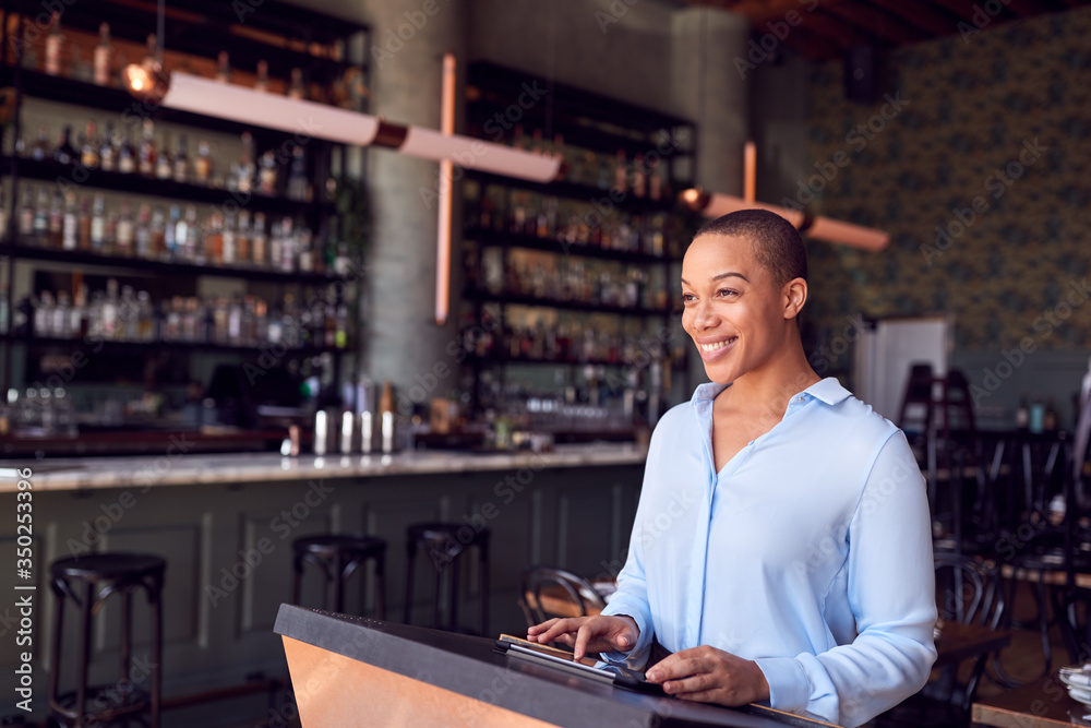 Female Owner Of Restaurant Bar Standing At Counter Using Digital Tablet Female Owner Of Restaurant Bar Standing At Counter Using Digital Tablet